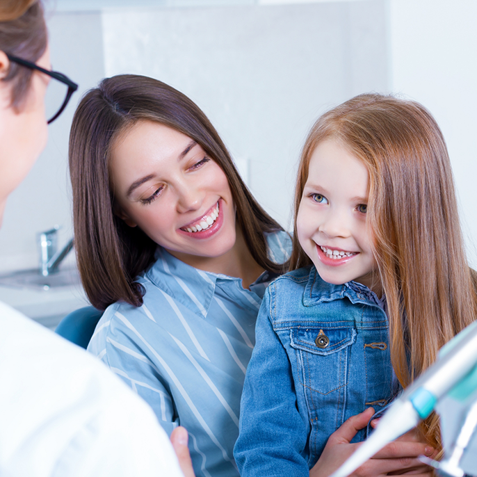 Woman in orthodontist's chair holding a little girl