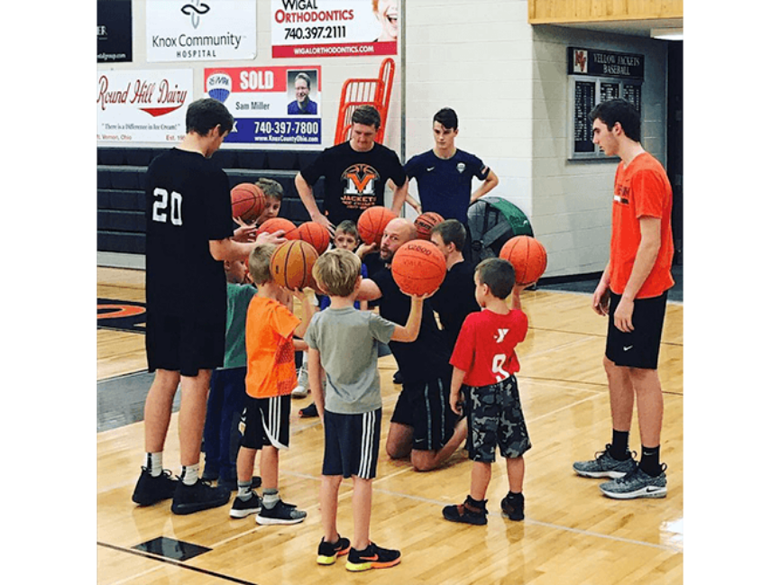 Kids holding basketballs surrounded by coaches