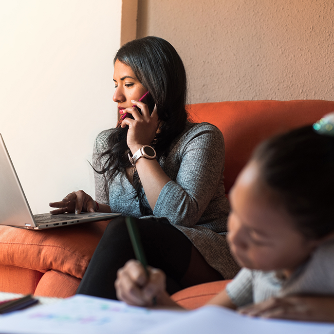 Woman on couch working on laptop and talking on phone