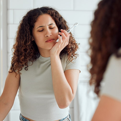 Woman holding toothbrush holding jaw in pain