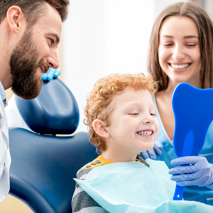 Child with orthodontist and parent checking smile in mirror